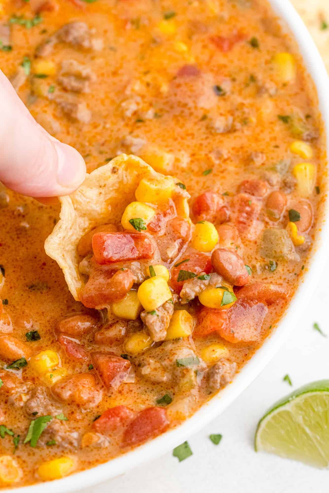 Chip being dipped into large bowl of chili.