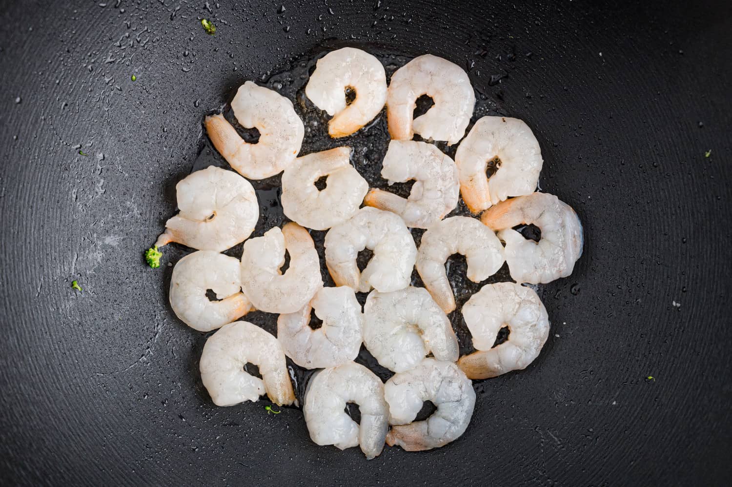 Uncooked shrimp in a single layer in a black pan.