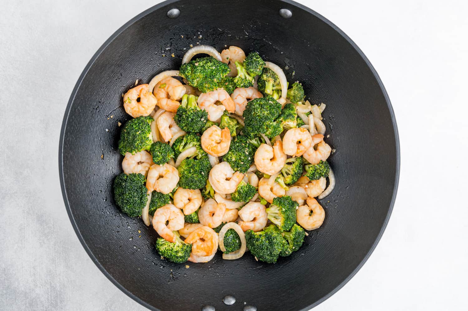 Shrimp, broccoli, onions, and sauce in a black wok.