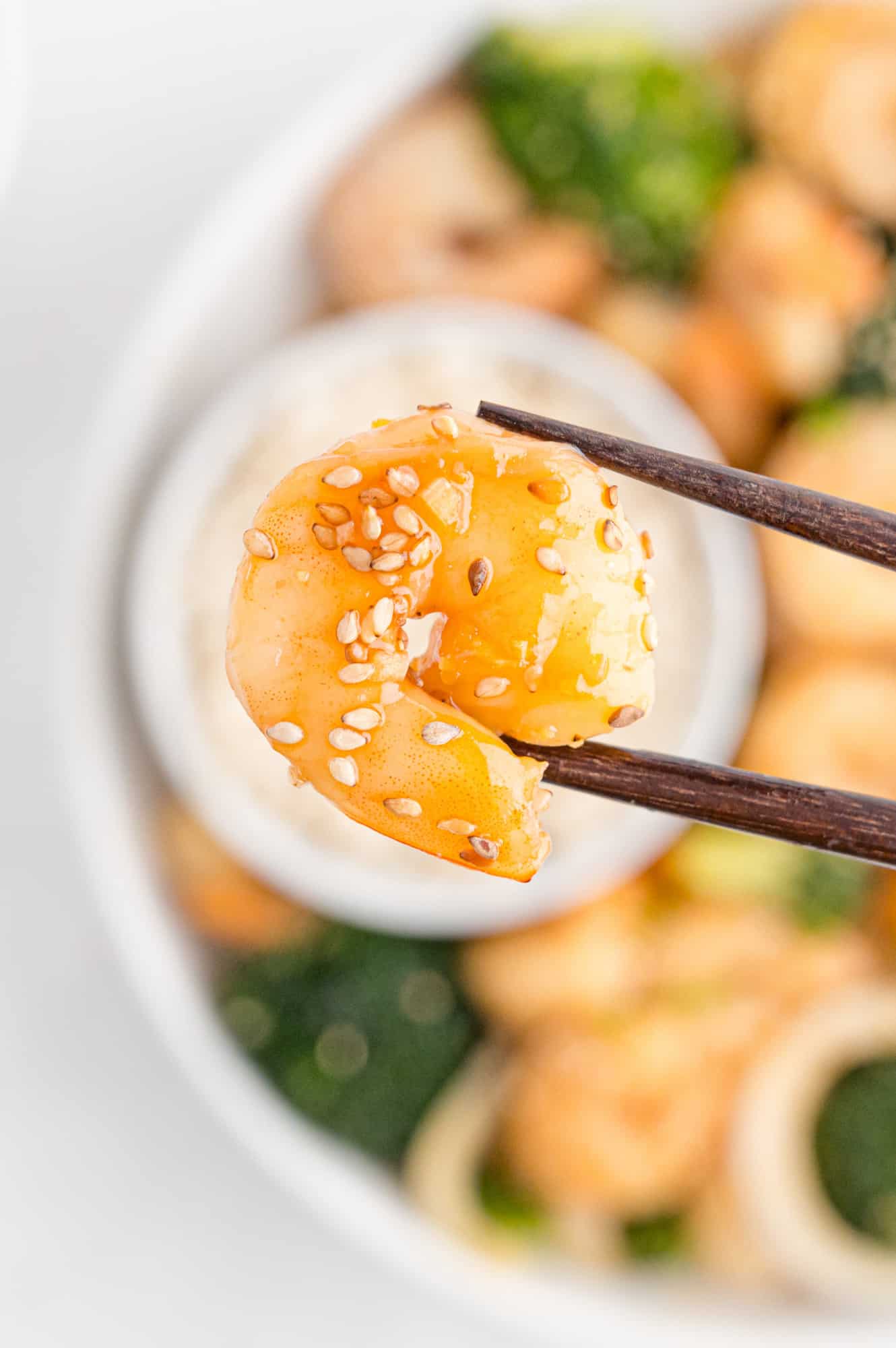 Shrimp with sauce and sesame seeds, held between chopsticks.