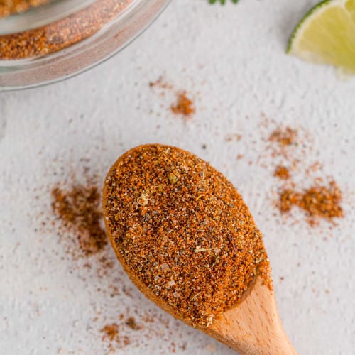 Taco seasoning on a small wooden spoon with some spilling off.