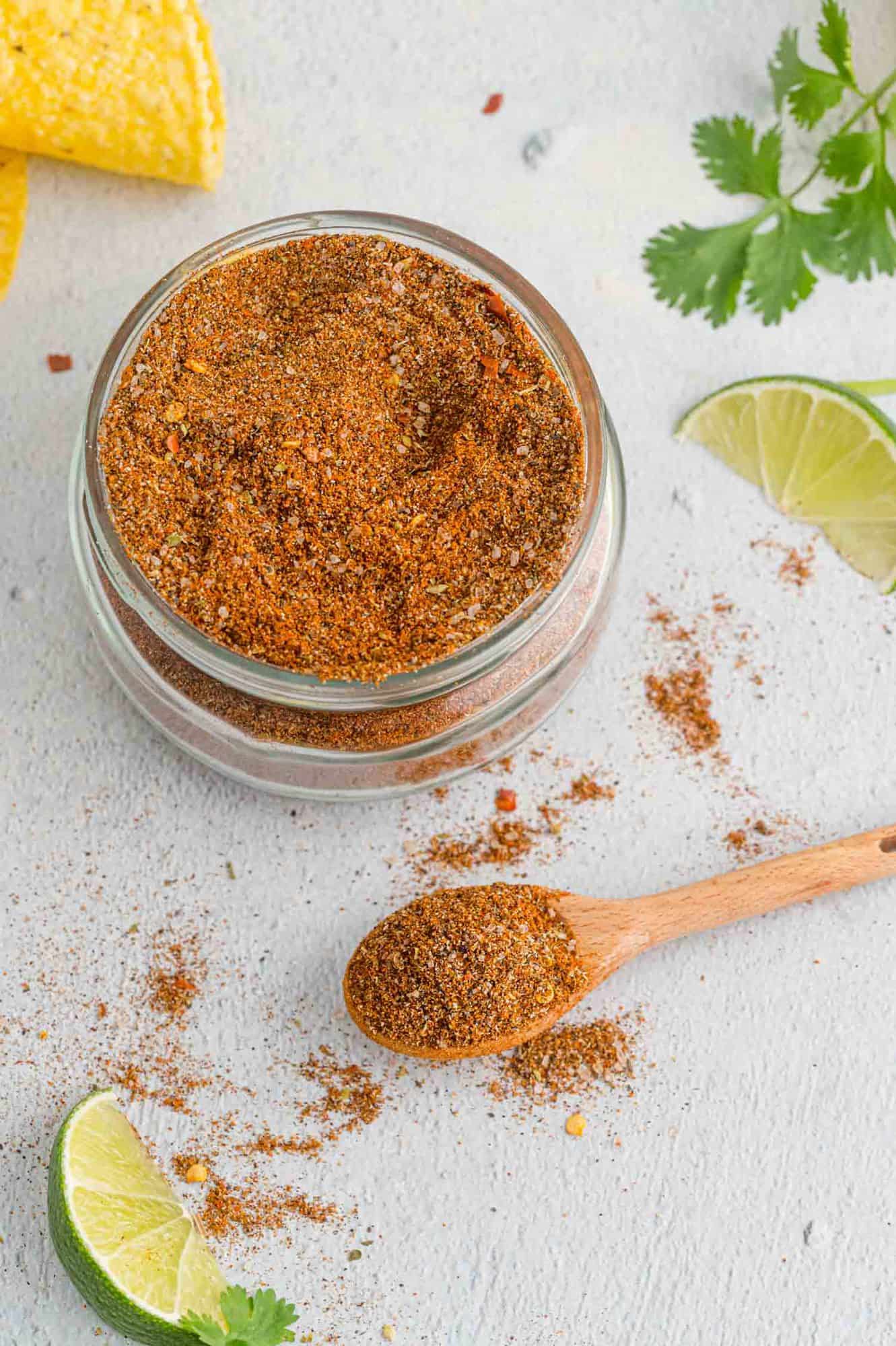 Taco seasoning in a small jar, a wooden spoonful nearby, and a lime wedge.