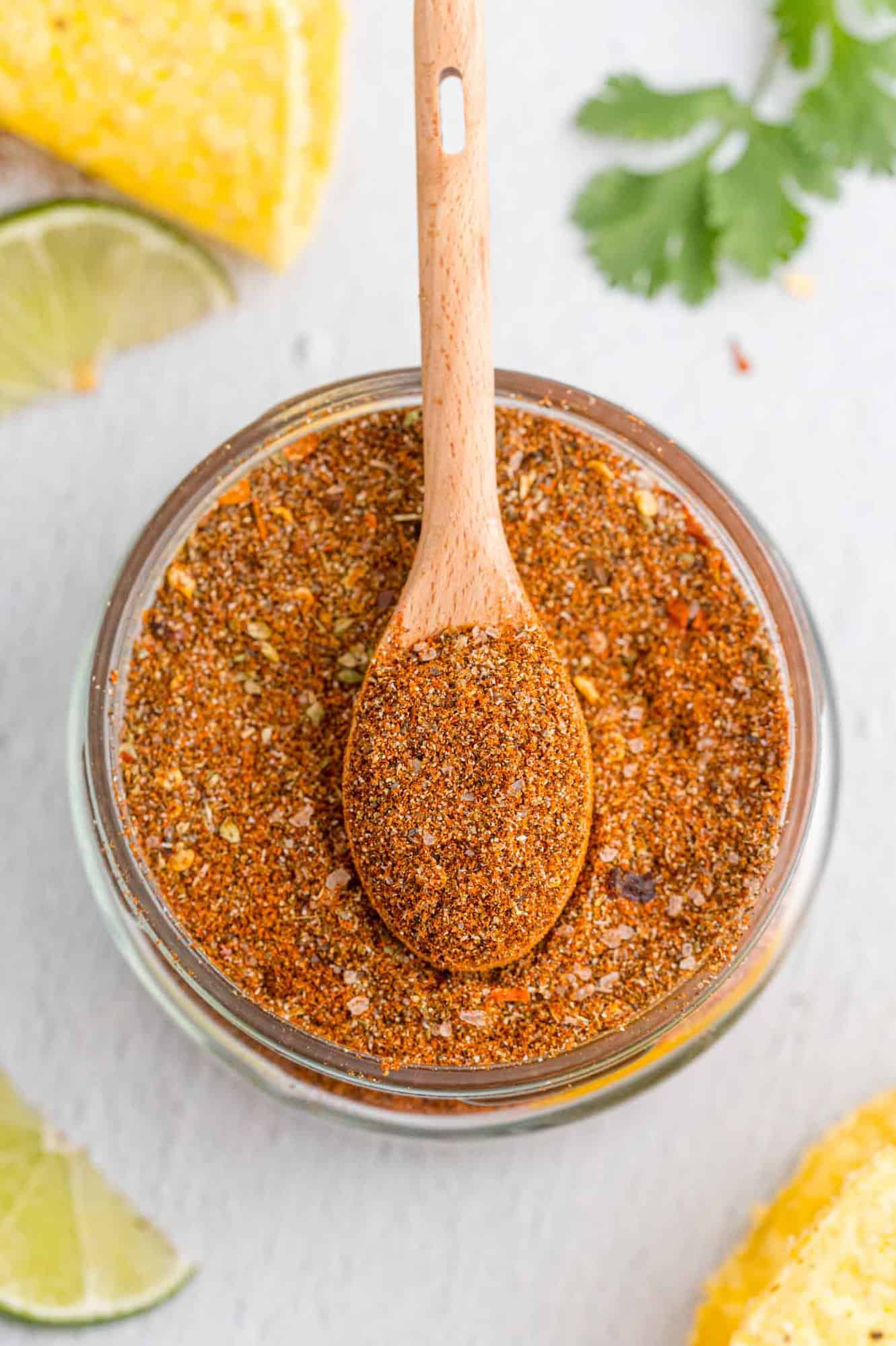 Overhead view of seasoning for tacos in a small glass jar with a wooden spoon.