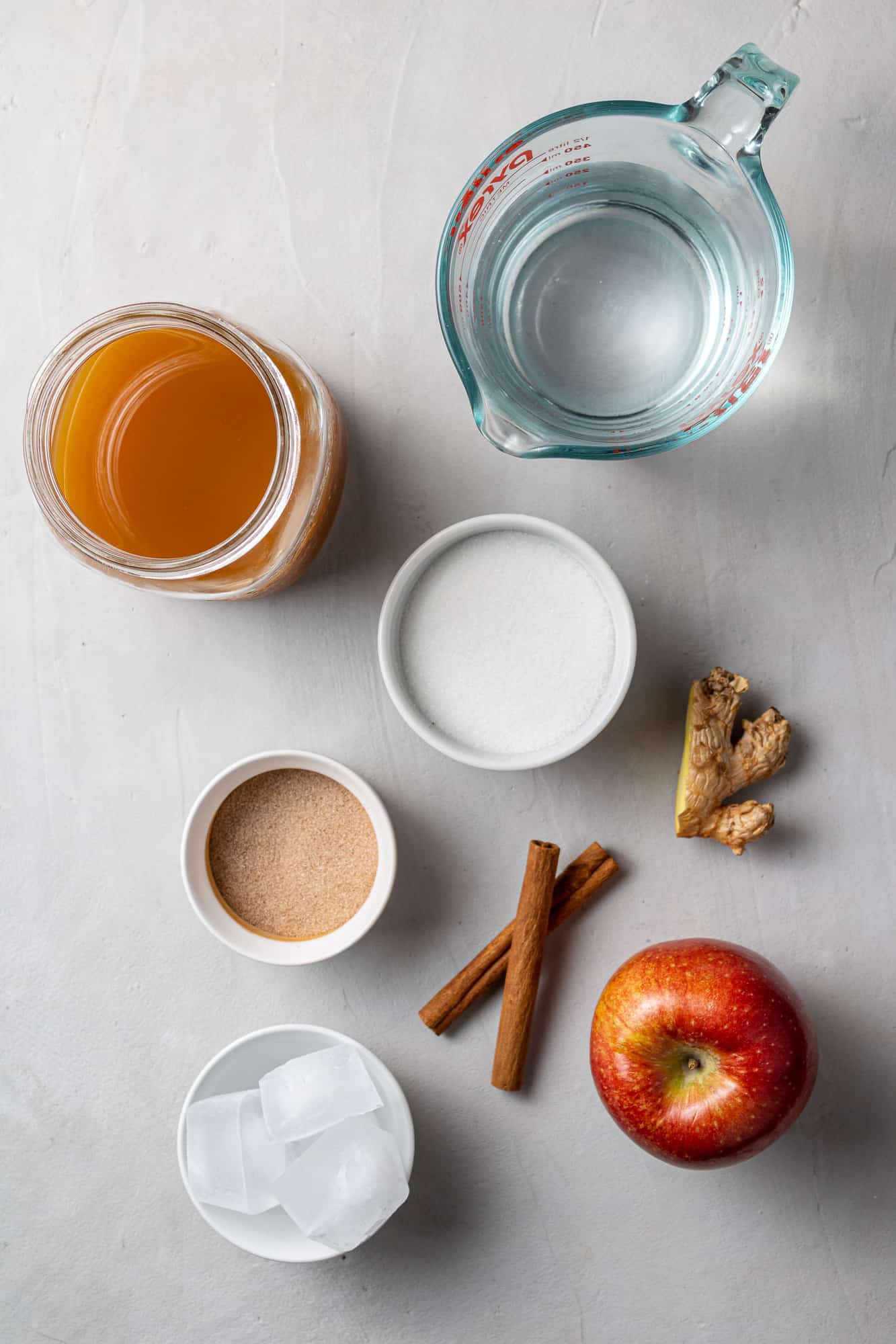 Overhead view of cider, water, cinnamon sticks, ginger, apple, and cinnamon sugar.