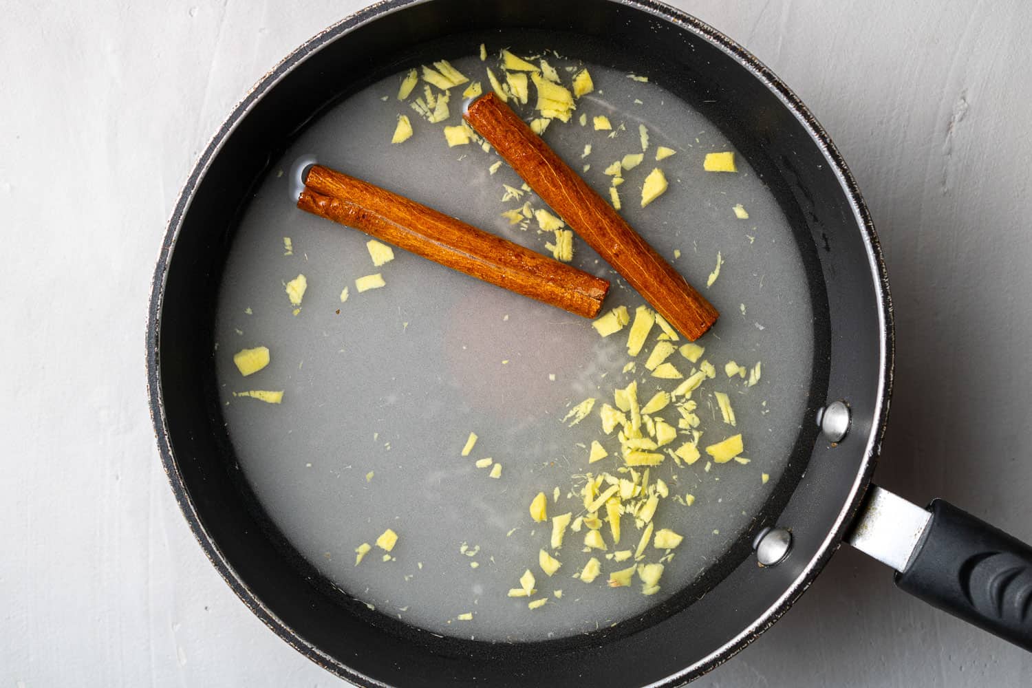 Overhead view of black pan with water, sugar, ginger, and cinnamon.