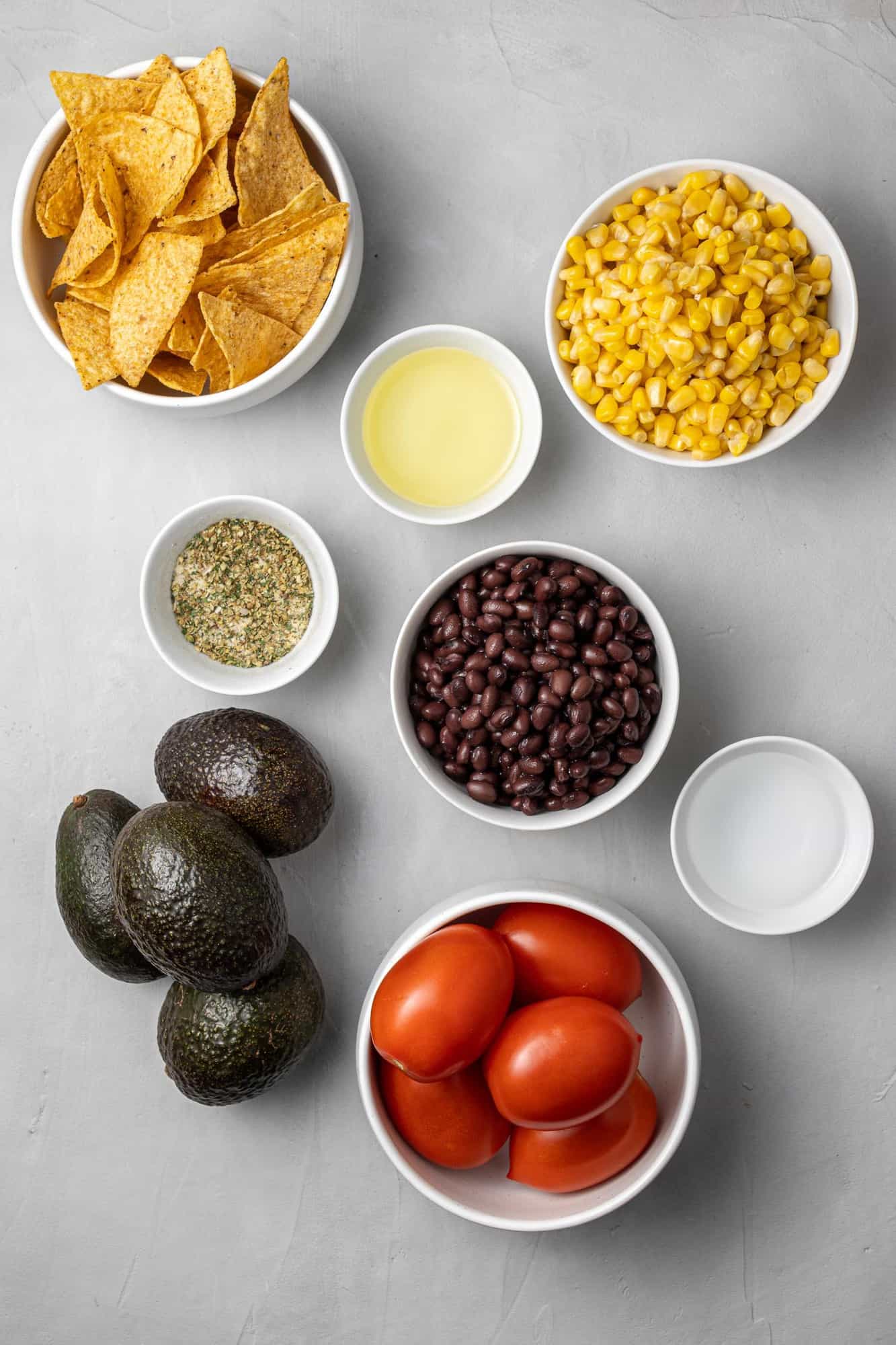 Overhead view of ingredients: tomatoes, corn, avocados, beans, chips.