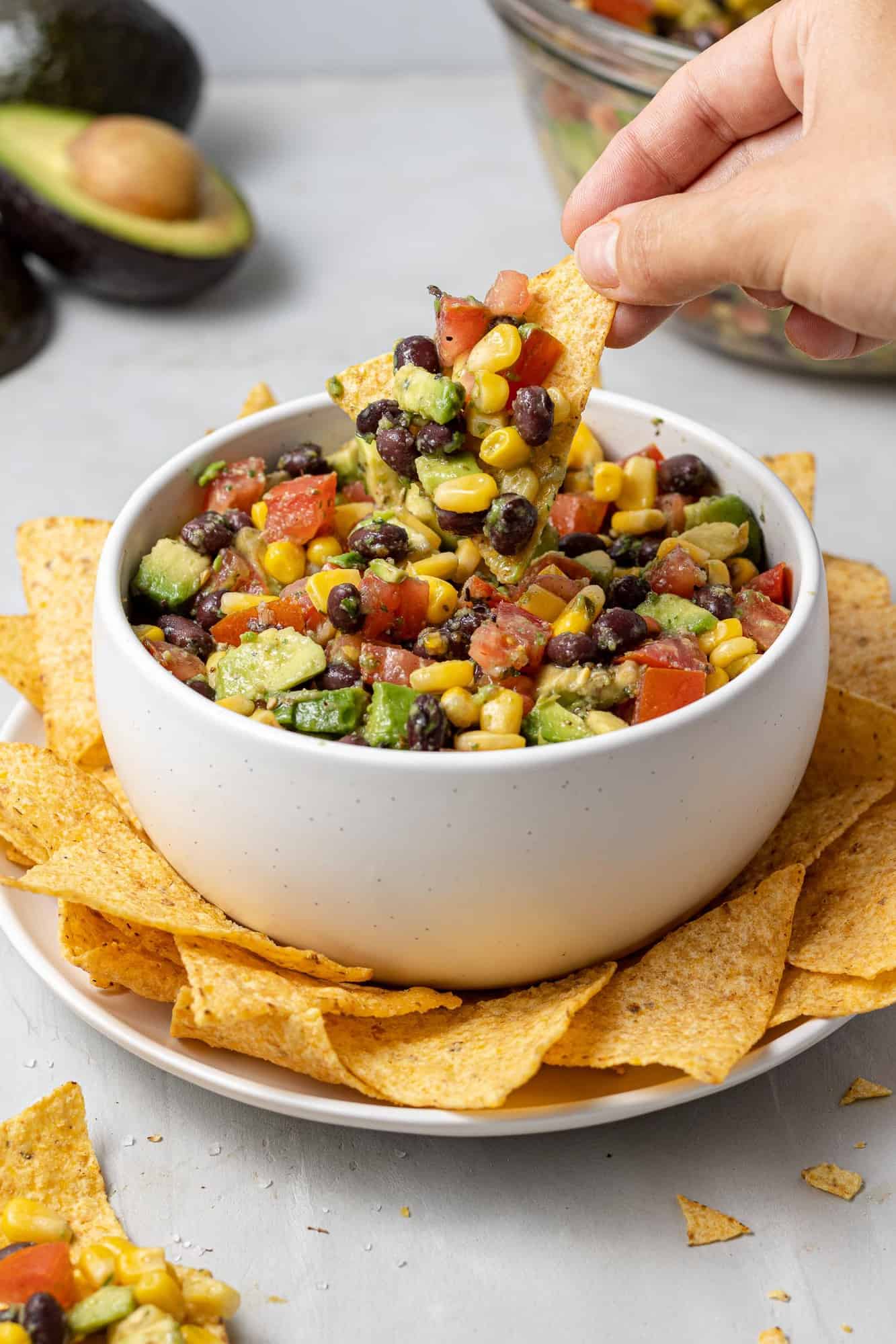 Chip dipping into a bowl of avocado, tomatoes, black beans, and corn.