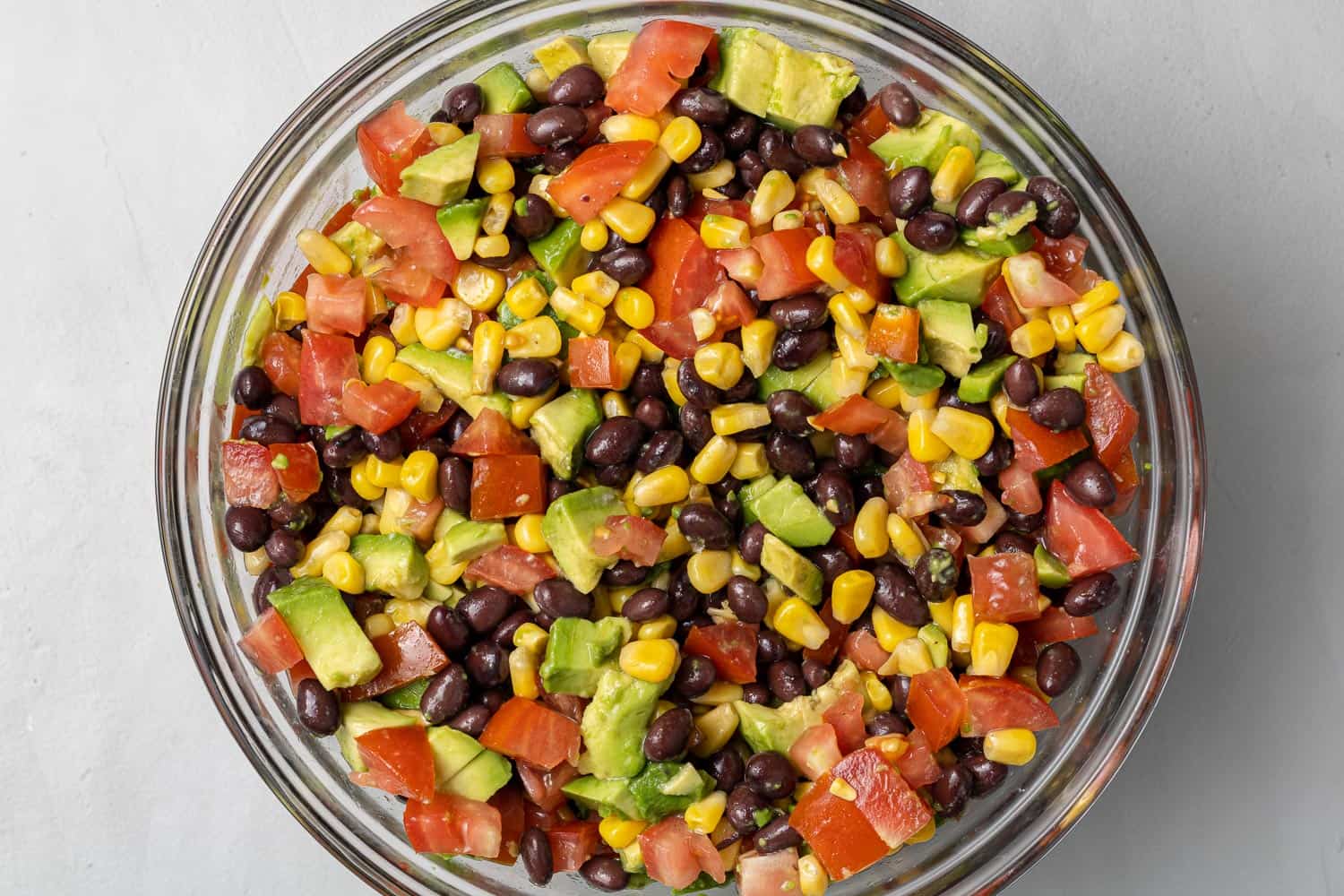 Chopped vegetables, avocado, and beans in a white glass bowl.