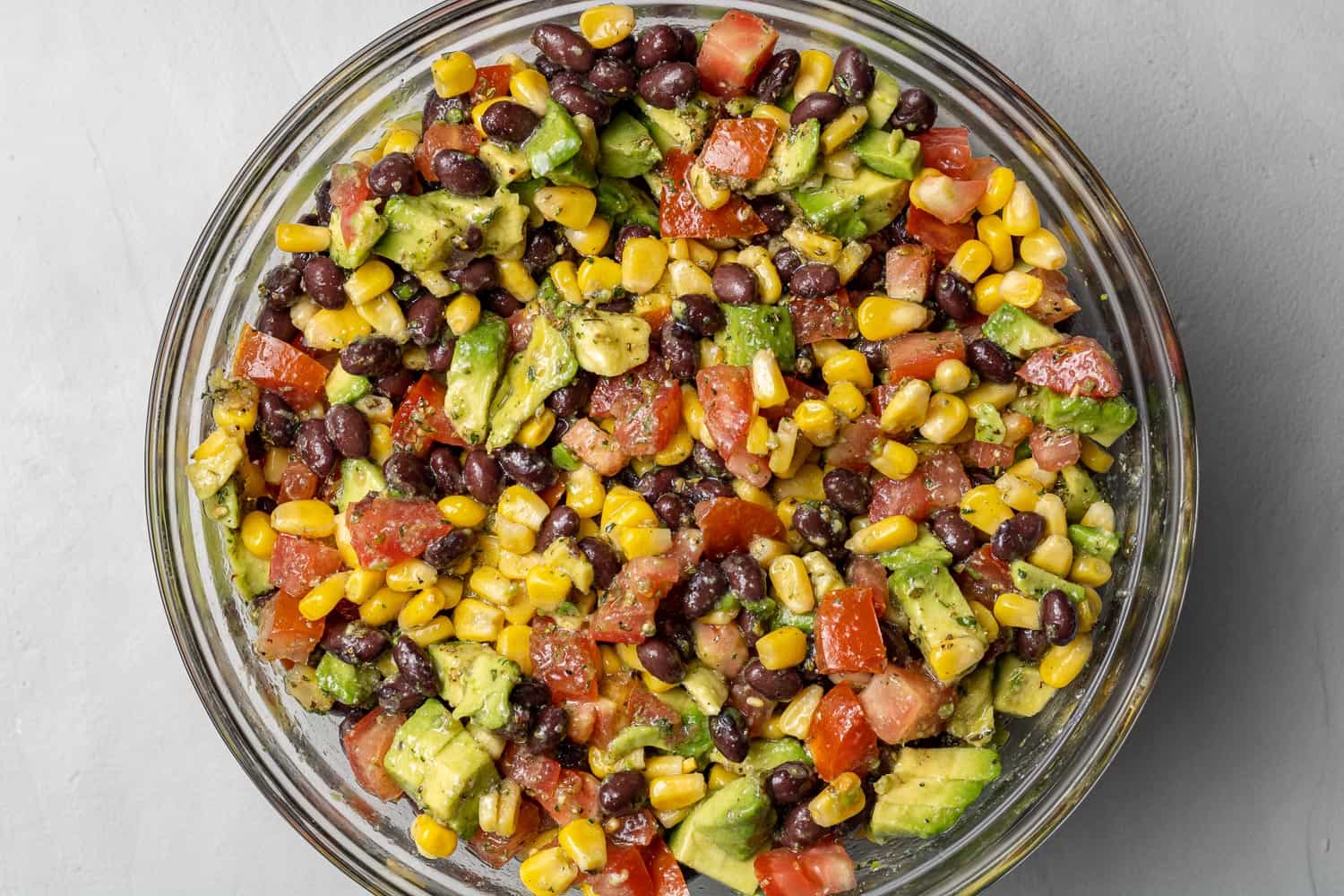 Avocado and black bean salad in a large clear glass mixing bowl.