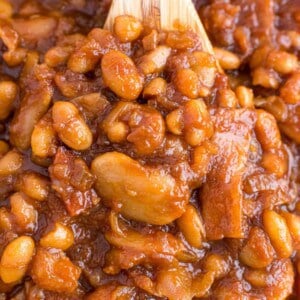 Close up view of baked beans on a wooden spoon.