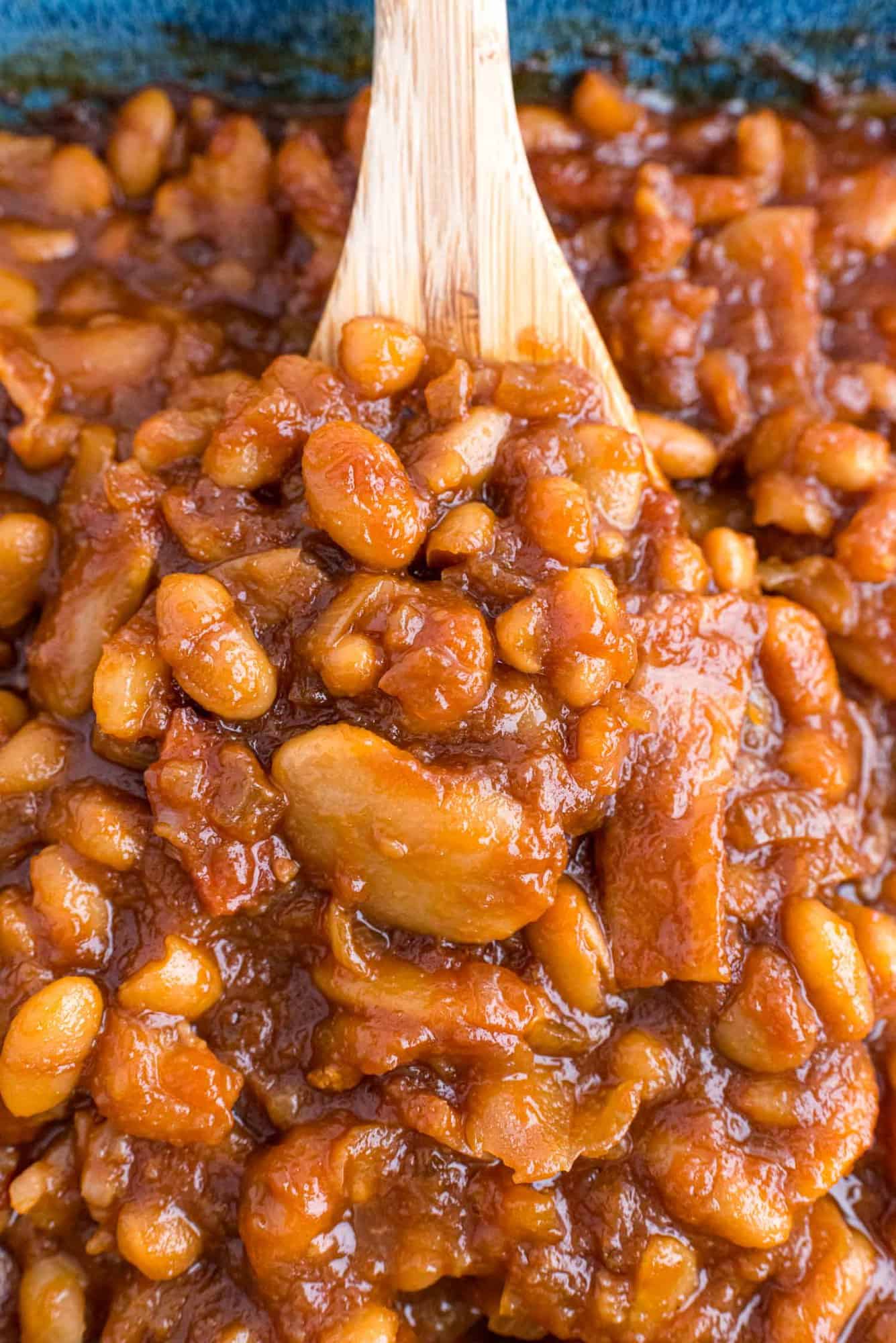 Close up of homemade baked beans with bacon on a wooden spoon.