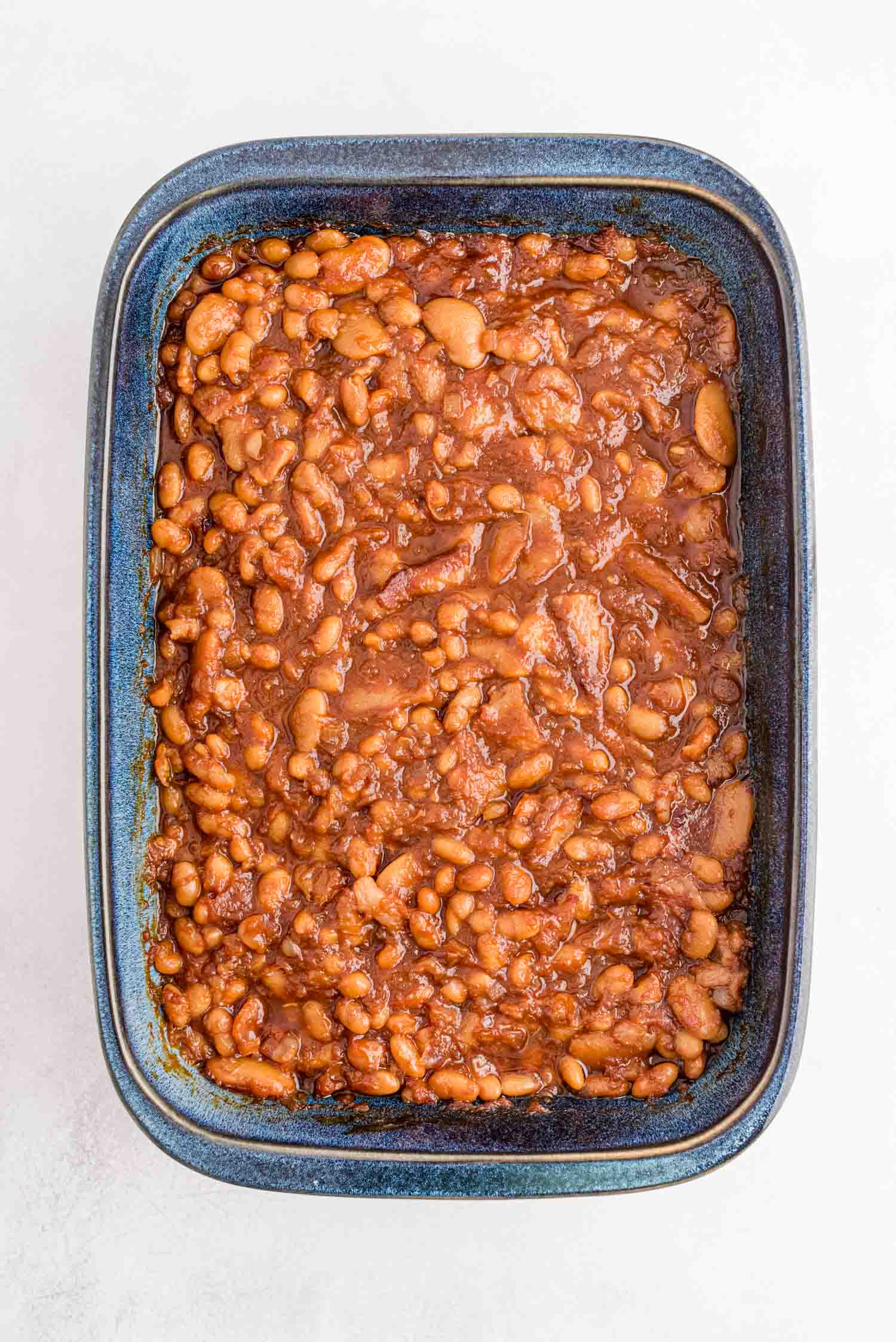 A blue rectangular baking dish filled with baked beans in a thick, reddish-brown sauce.