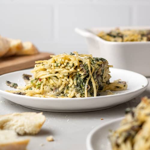 Baked spaghetti with spinach on a small round white plate.