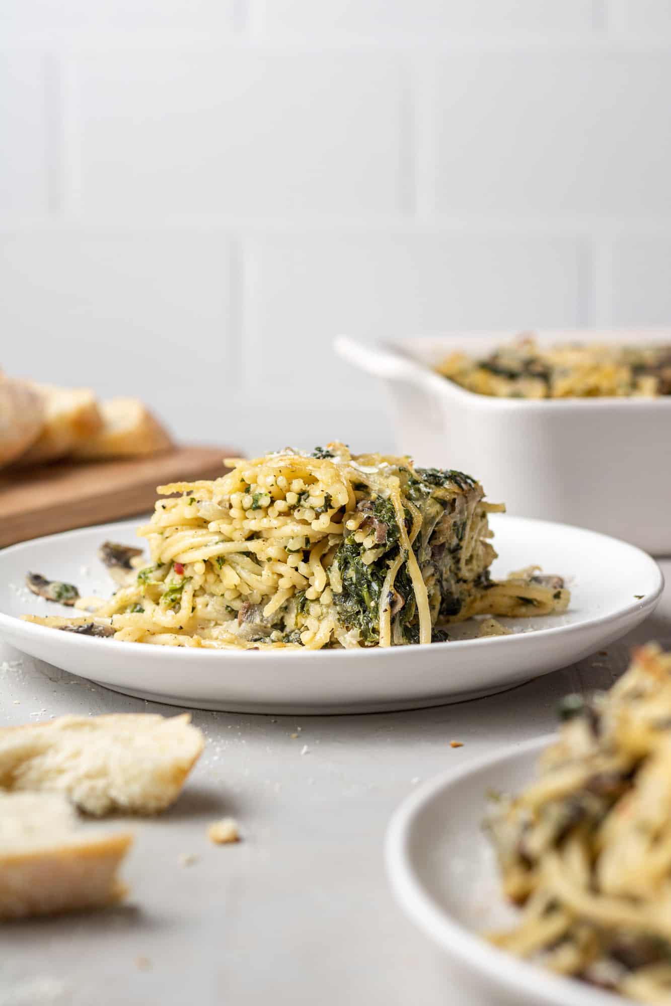 Square of baked spaghetti on a plate with casserole dish in the background.