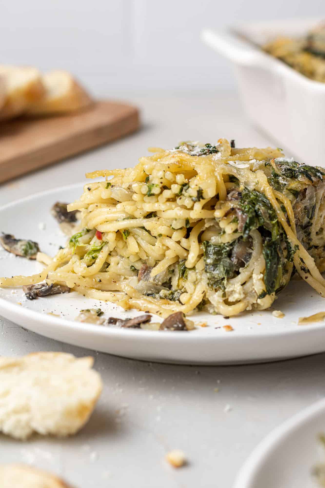 Close up of spaghetti mixed with spinach, cheese, and mushrooms on a small white plate.