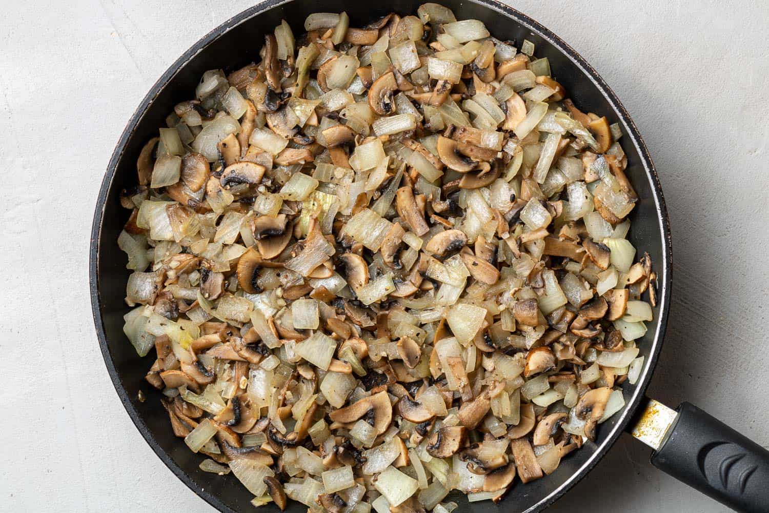 Sautéed mushrooms and onions in a black frying pan.