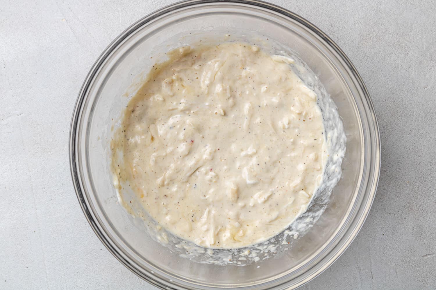 Cheese mixed with sour cream, egg, and seasoning in a glass bowl.