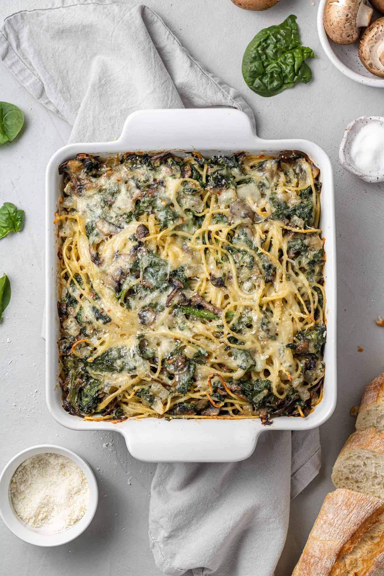 Baked spaghetti with spinach and mushrooms in a square white baking dish.