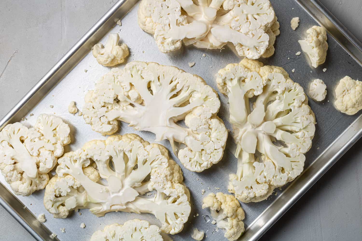 Cauliflower slices on a silver sheet pan.