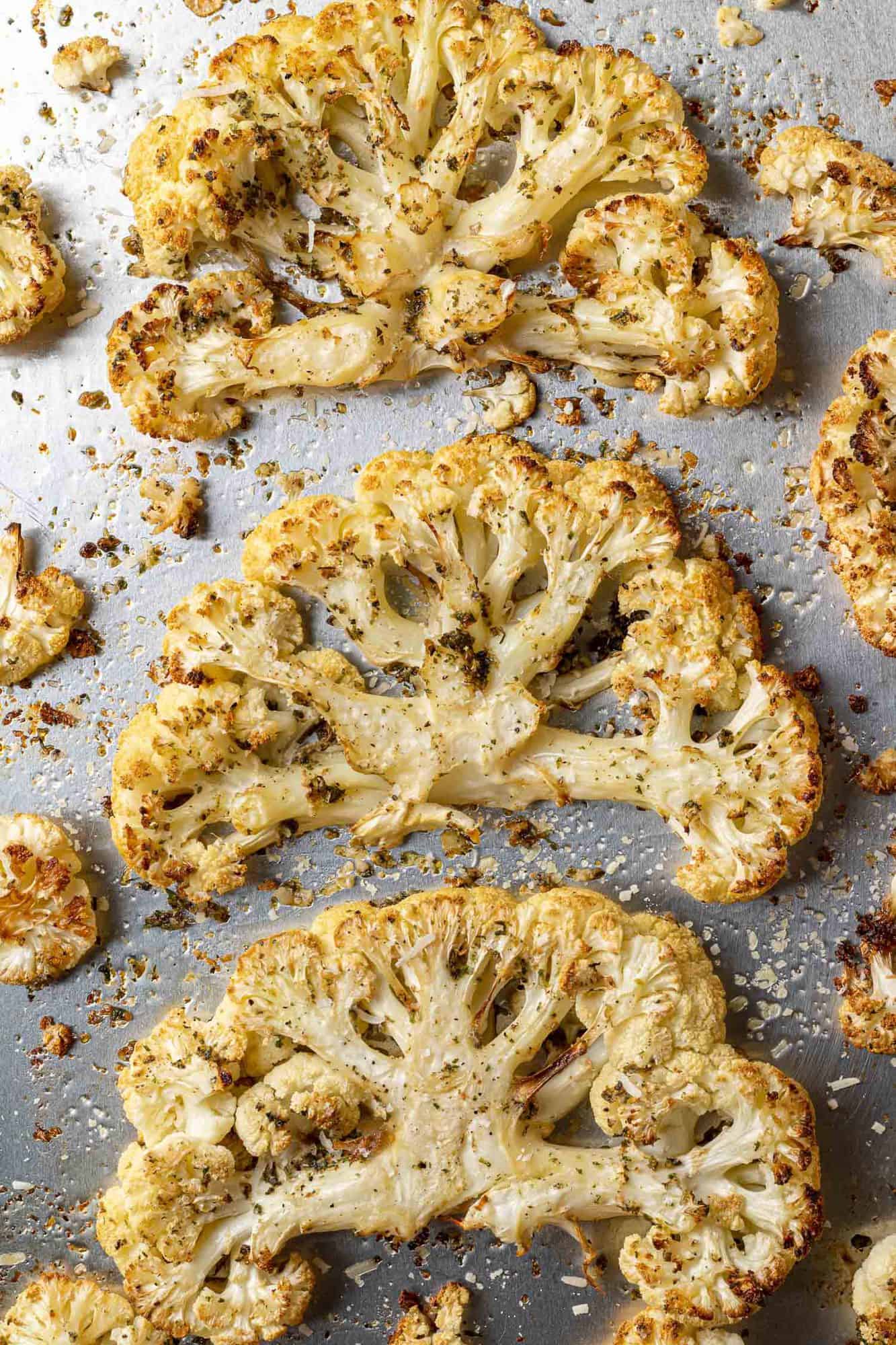 Overhead view of three large cauliflower steaks on a silver sheet pan.