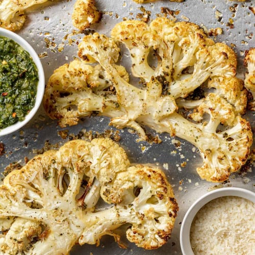 Overhead view of cauliflower steaks on a sheet pan with parmesan and chimichurri.