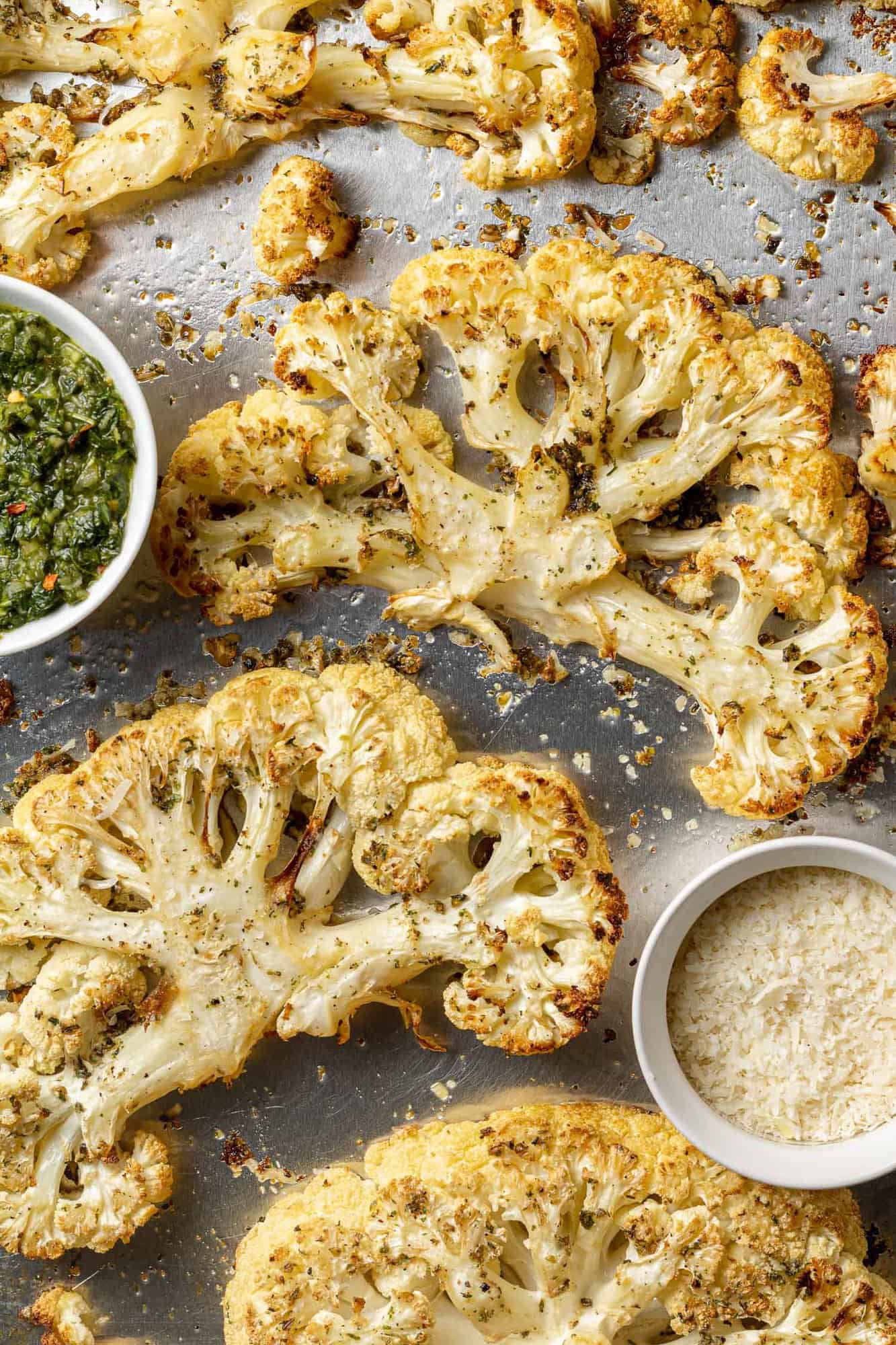 Cauliflower steaks shown on a sheet pan with parmesan and chimichurri.