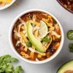 Overhead view of a bowl of chicken tortilla soup topped with avocado, tortilla strips, and cheese.