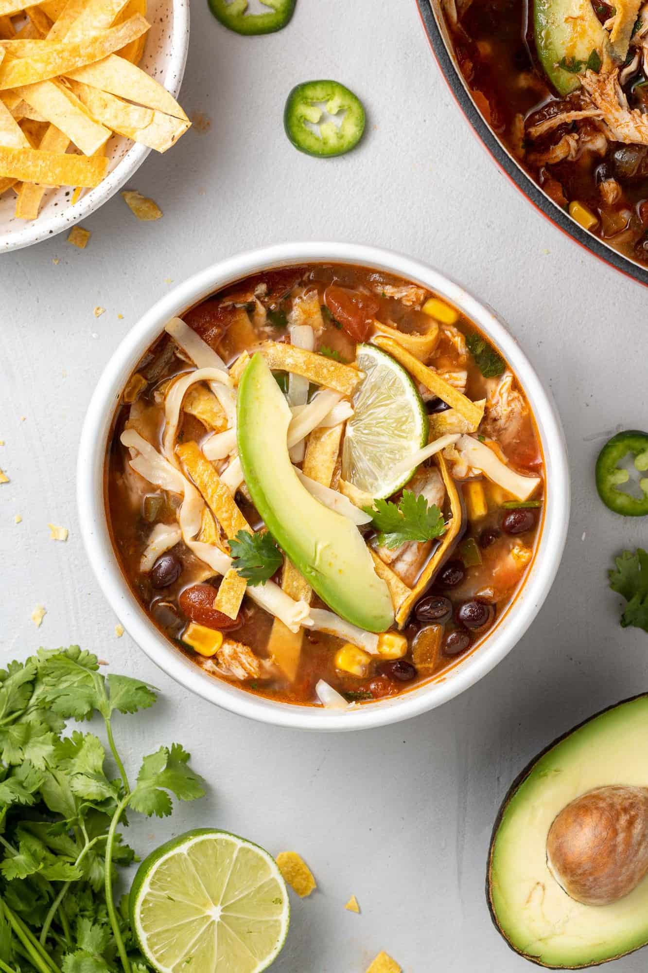 Overhead view of bowl of chicken tortilla soup topped with avocado, cilantro, tortilla strips.