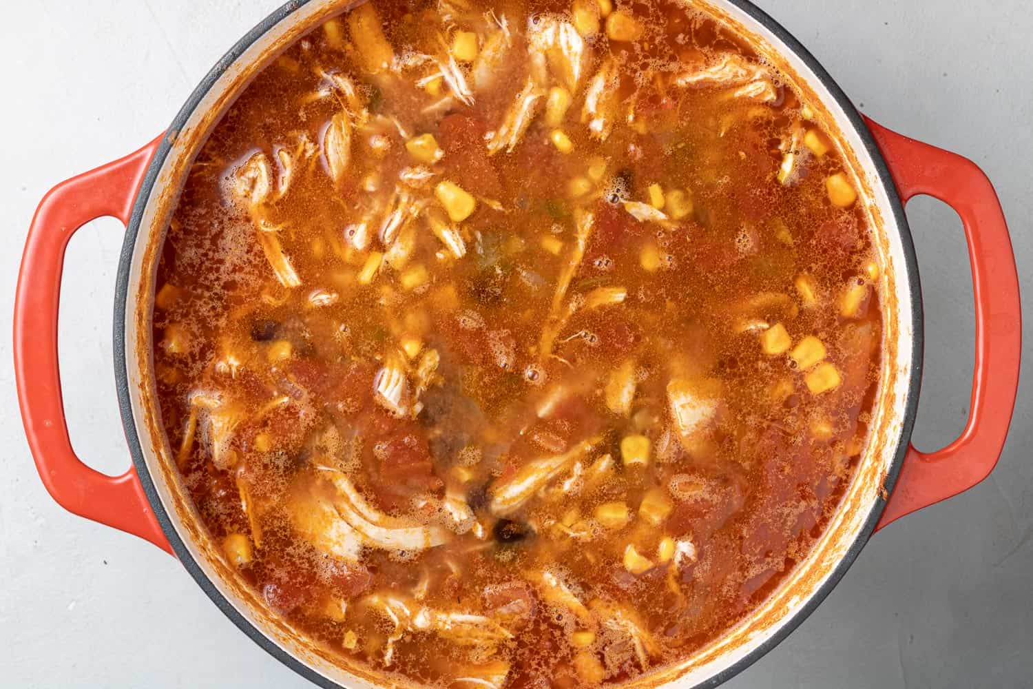 Tortilla soup in a red dutch oven with fresh corn added.
