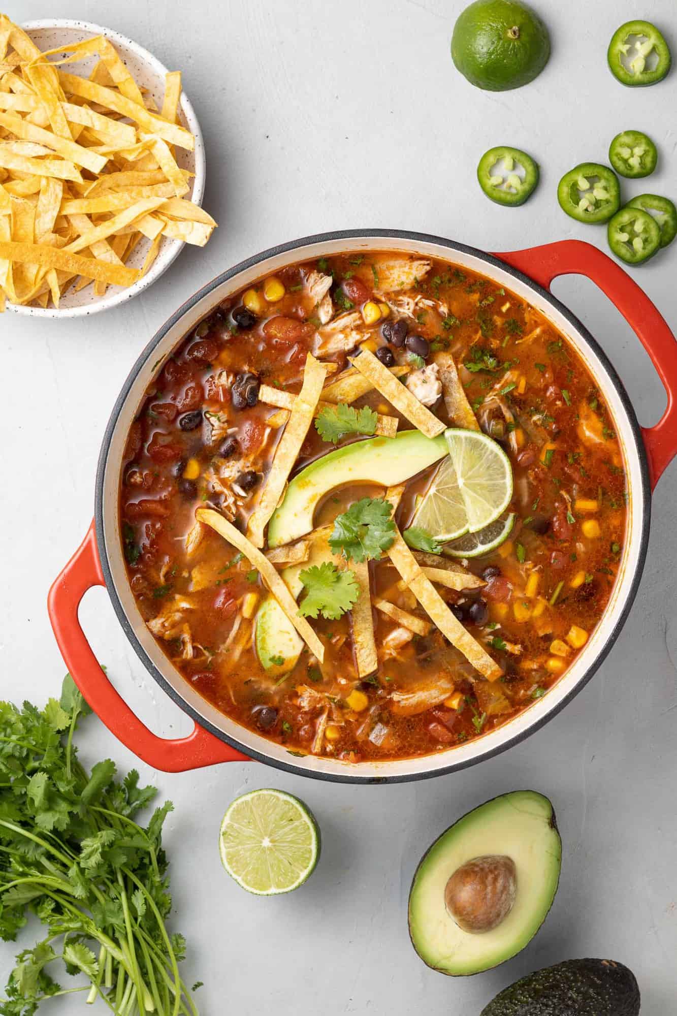 Large red dutch oven filled with chicken tortilla soup and fun garnishes.