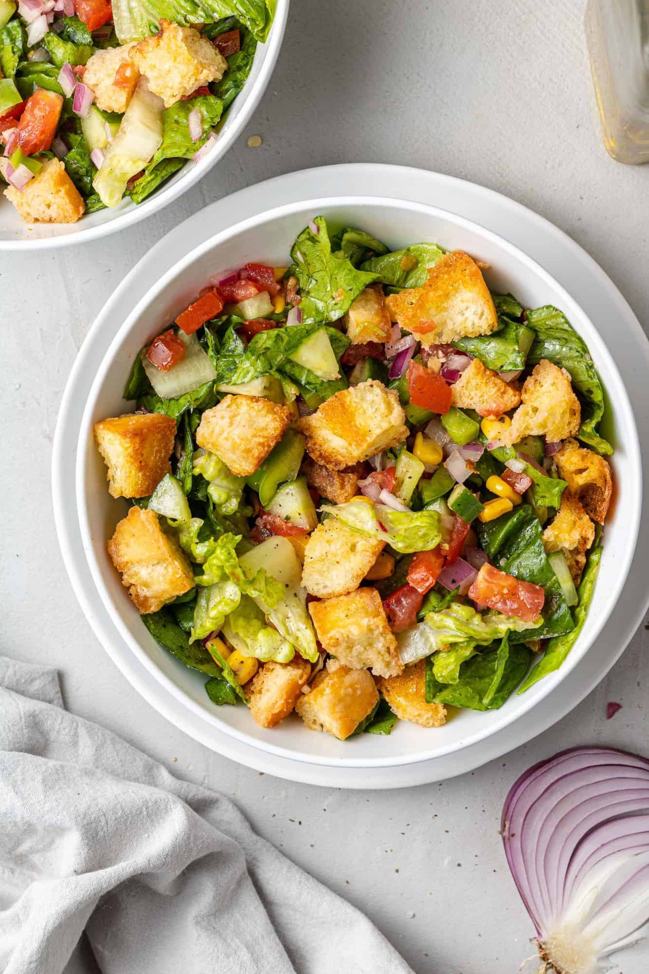 Overhead view of green salad with croutons in a white bowl.