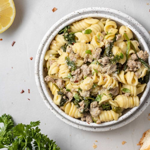 Overhead view of pasta with ground chicken, lemon, and spinach on a white plate.