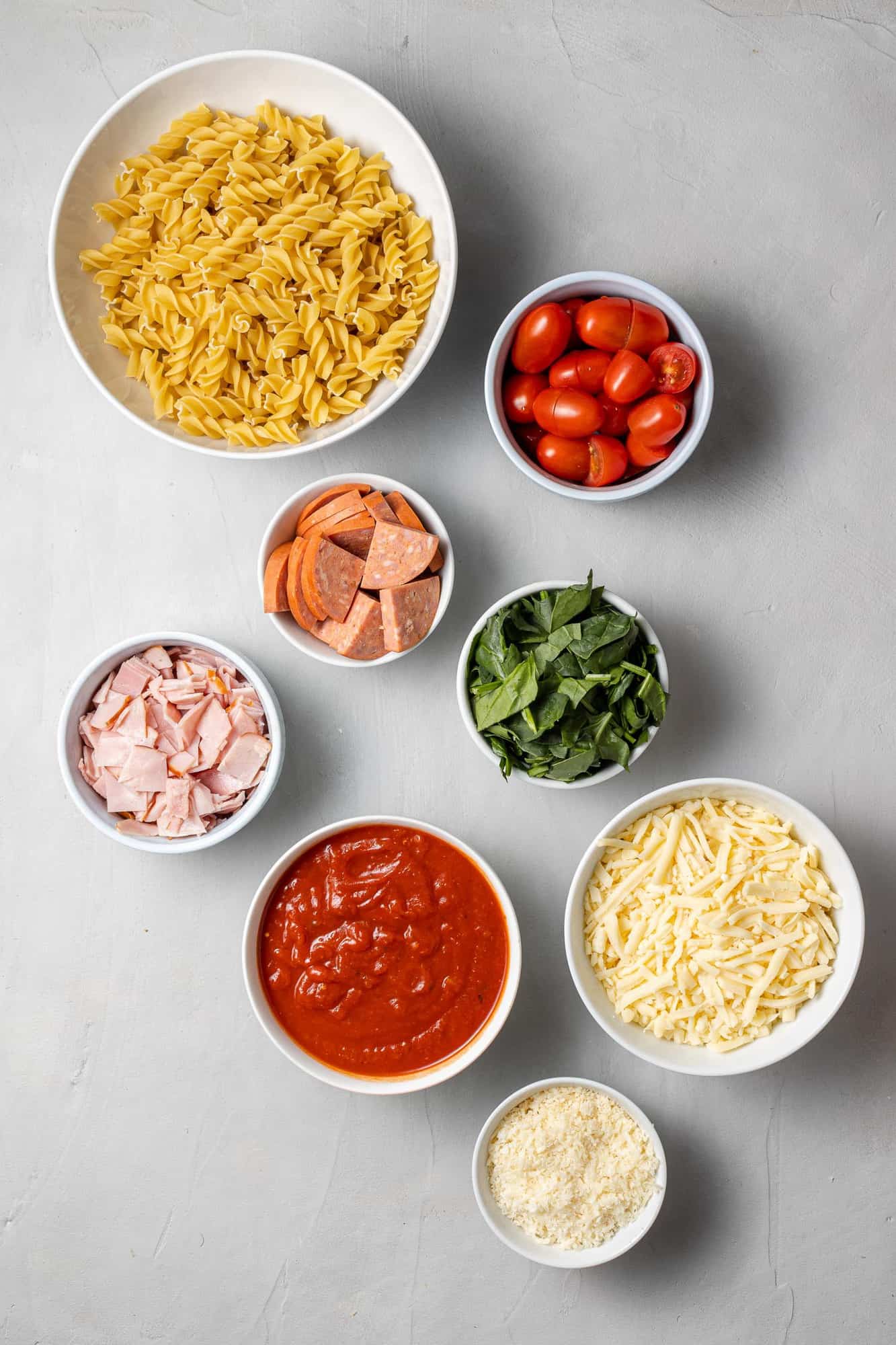 Overhead view of ingredients needed including pasta, tomatoes, ham, pepperoni.