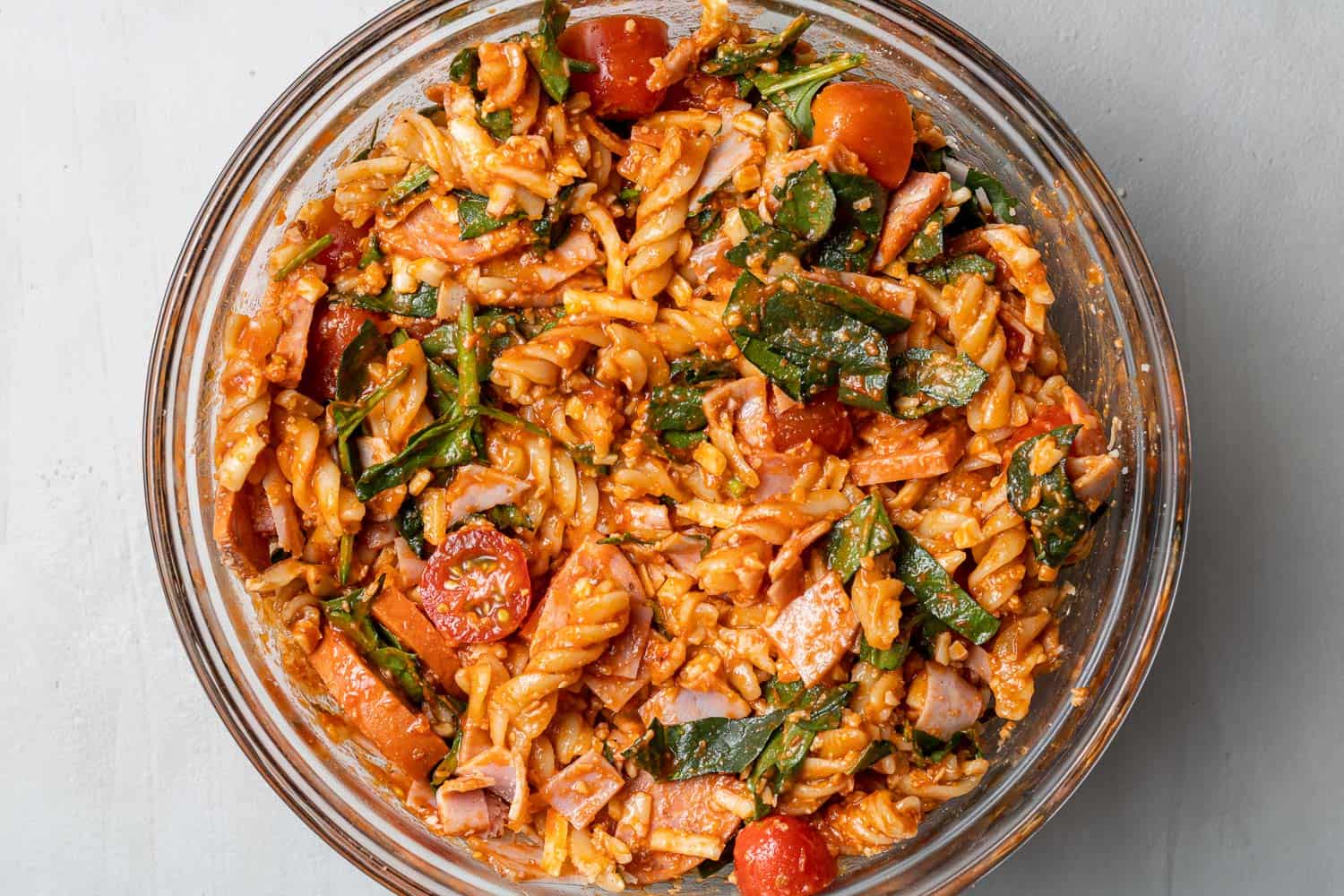 Pasta mixed with pizza sauce in a clear glass mixing bowl.