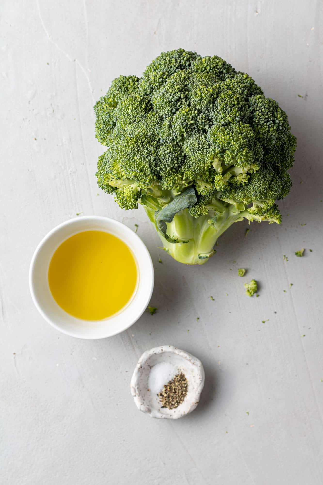 Overhead view of a head of broccoli, olive oil, salt, and pepper.