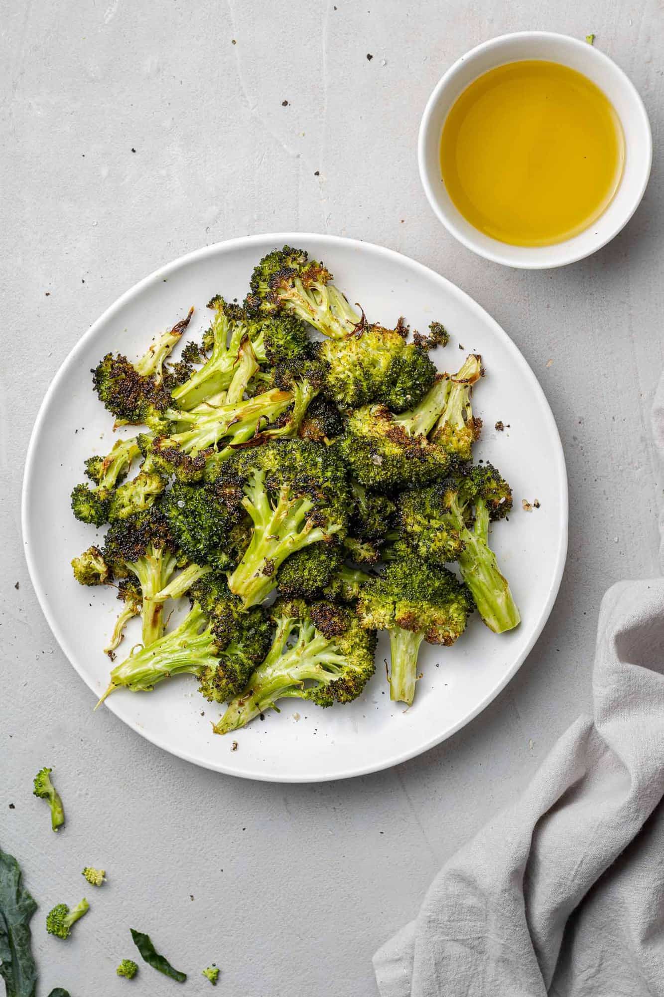 Roasted broccoli in a bowl, with a small bowl of olive oil nearby.