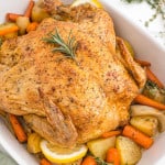Roasted chicken in a white baking dish with potatoes and carrots.