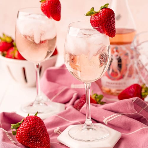 Two stemmed glasses with rose spritzers, garnished with strawberries.