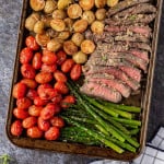 Cut steak, pink inside, on a sheet pan with tomatoes, potatoes, asparagus.