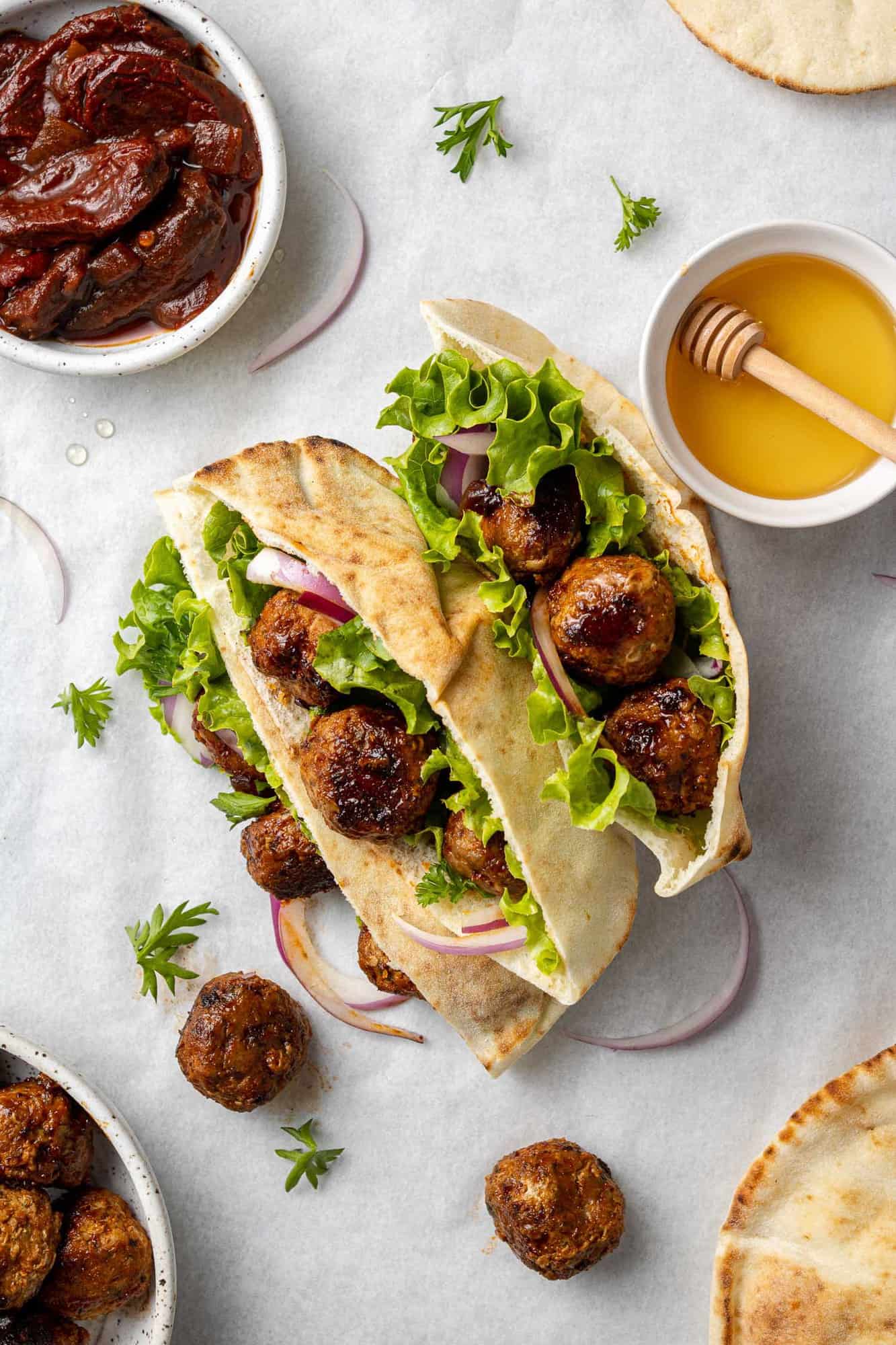 Overhead view of meatballs on a pita with lettuce, honey and chipotle chiles nearby.