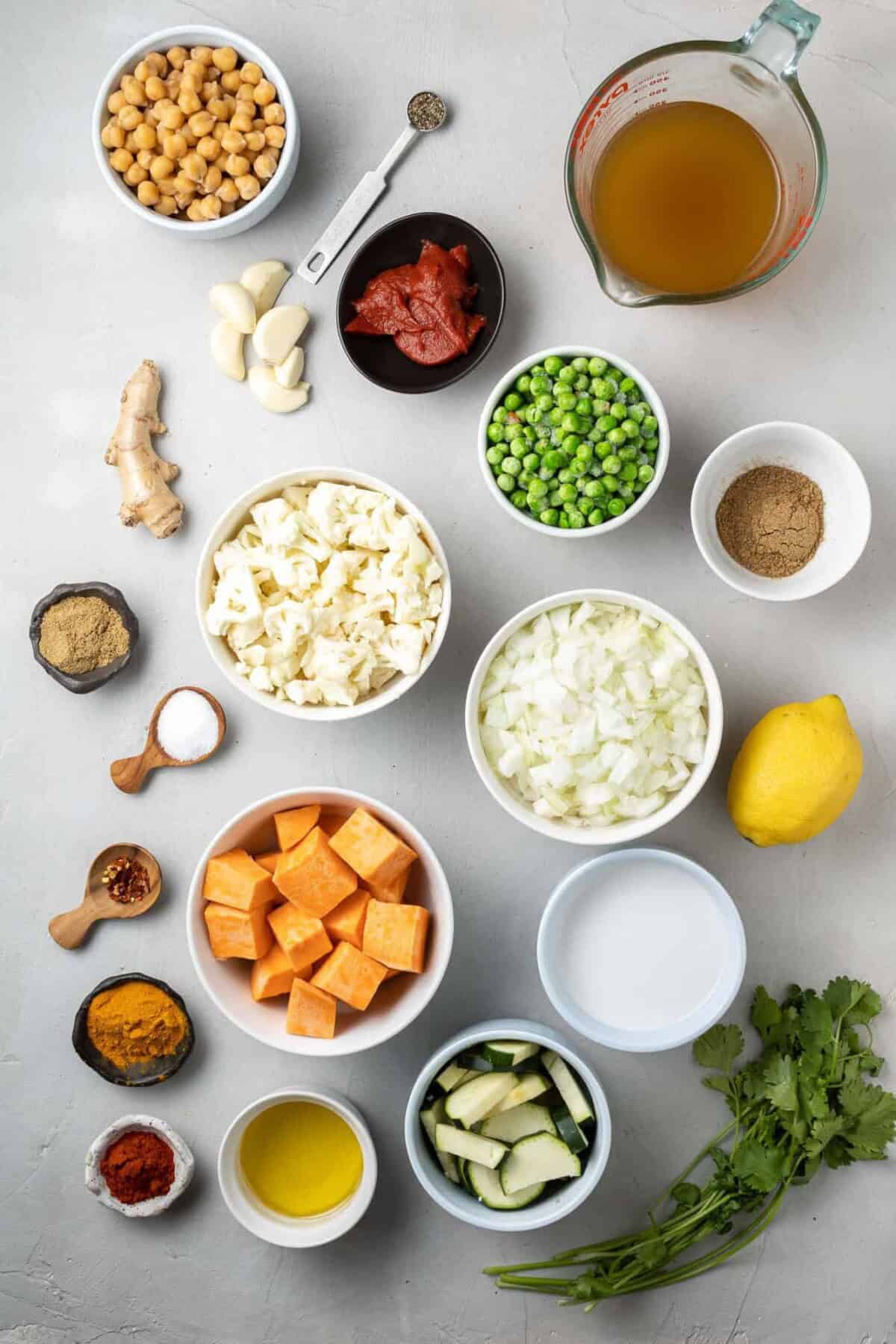 Overhead view of ingredients needed including spices, chickpeas, cauliflower, sweet potatoes, and peas.
