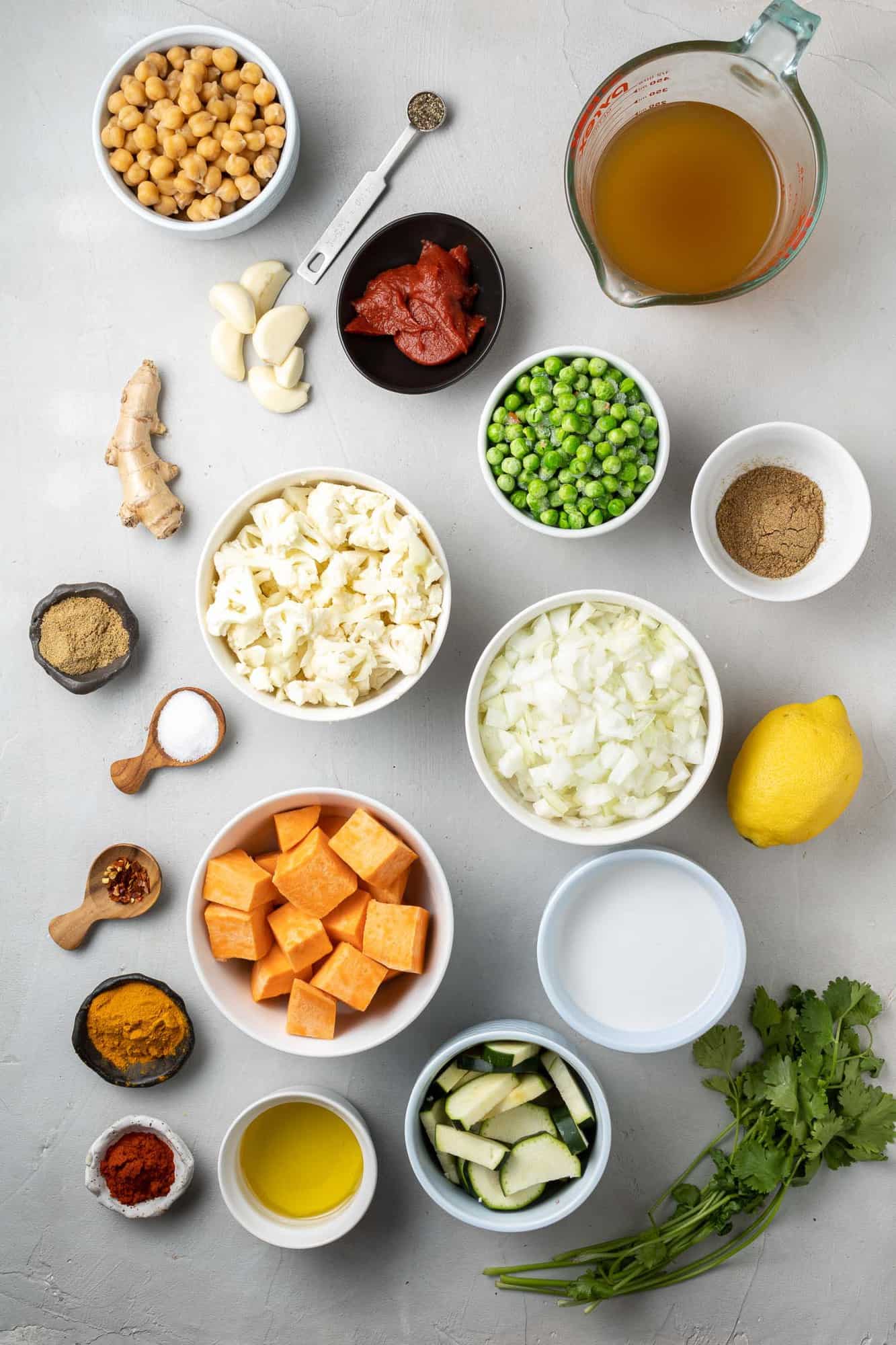 Overhead view of ingredients needed including spices, chickpeas, cauliflower, sweet potatoes, and peas.