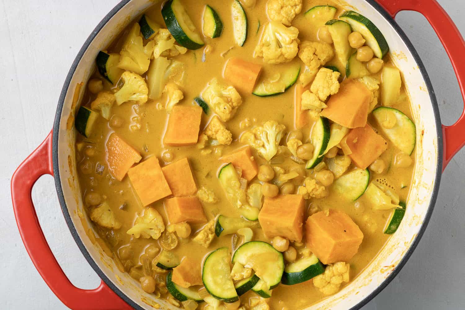 Uncooked vegetarian curry in a red dutch oven on a gray background.