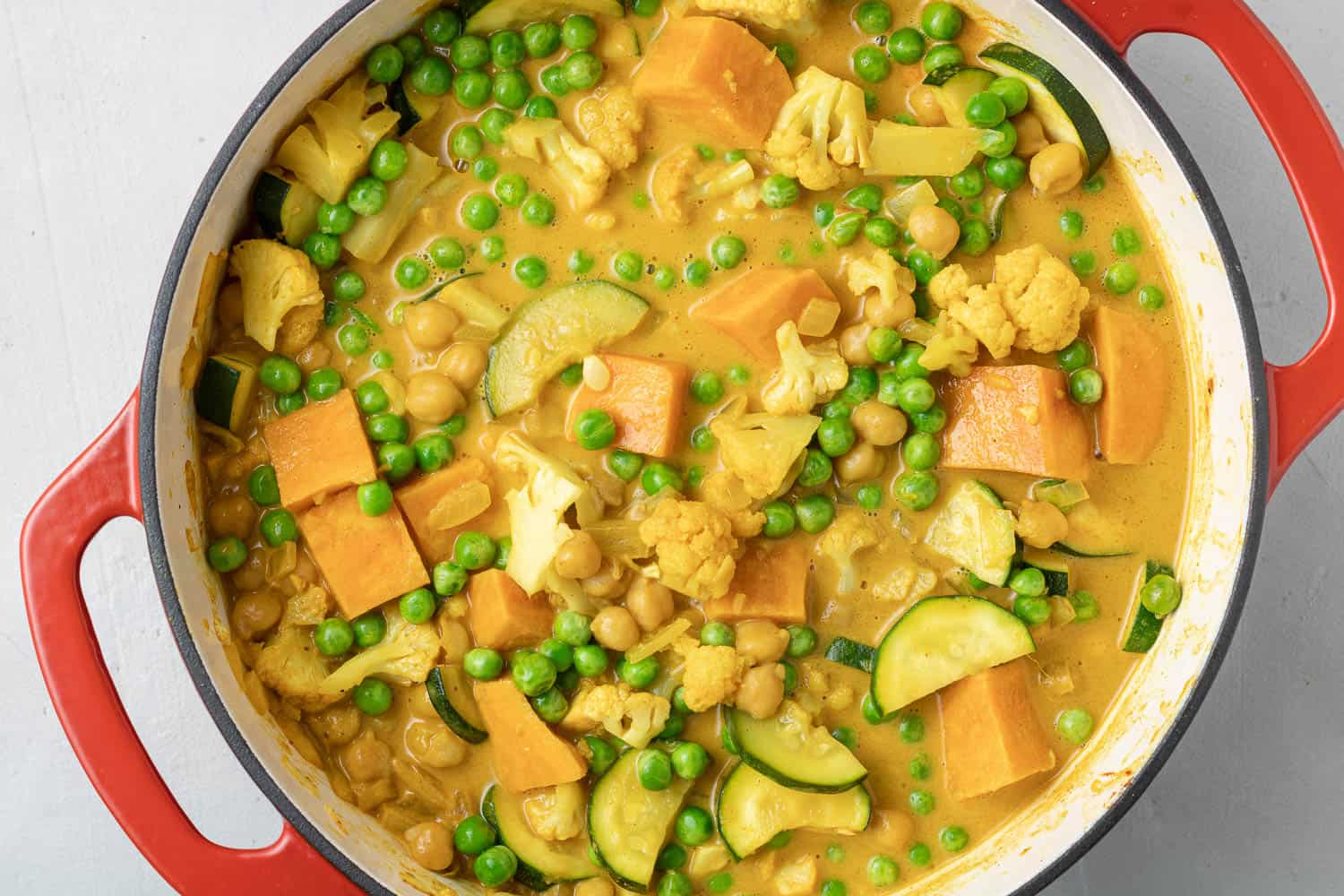 Peas added to a yellow orange curry in a red dutch oven.