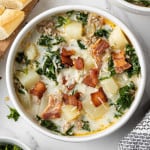 Overhead view of zuppa toscana soup in a white bowl garnished with crispy bacon.