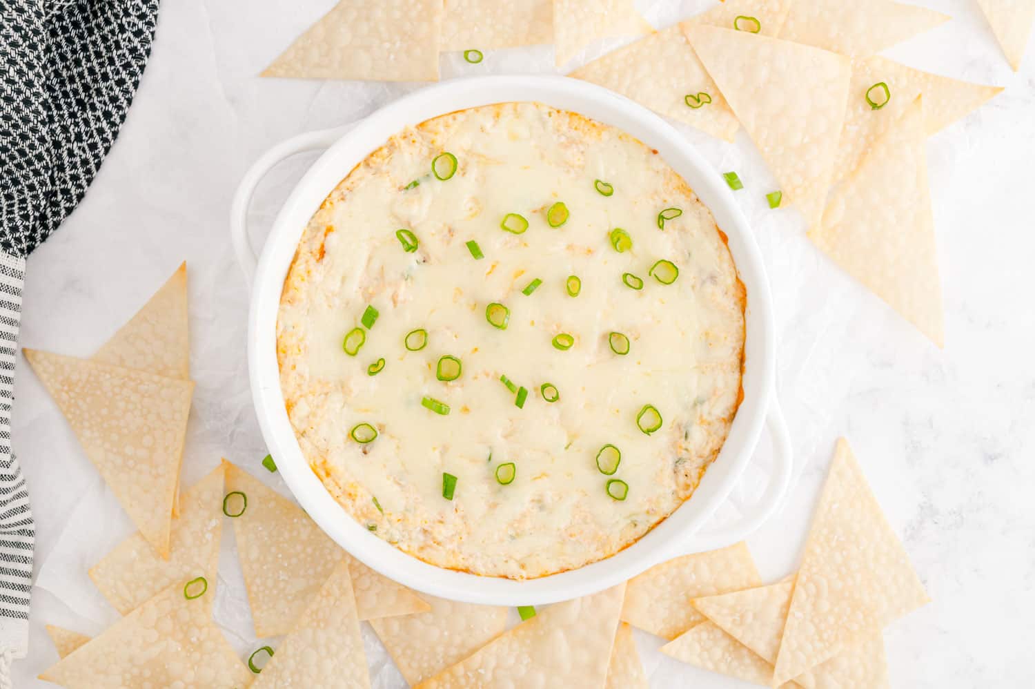 Dip, garnished with green onions, surrounded by wonton triangles.