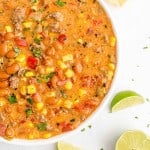 Overhead view of colorful creamy queso chili in a white bowl on a white surface.