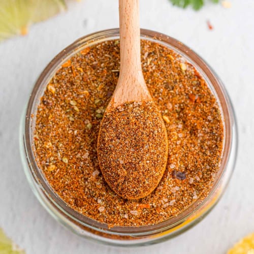 Overhead view of jar of taco seasoning with a wooden spoon in it.