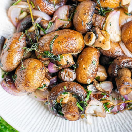 Cooked mushrooms with shallots and herbs, in a white bowl.