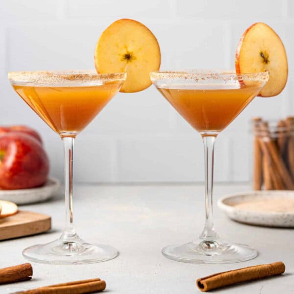 Two apple cider mocktails garnished with round apple slices.